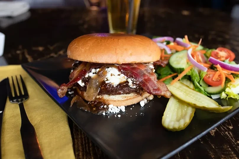 Gourmet burger with bacon, cheese, caramelized onions, salad, and pickles.
