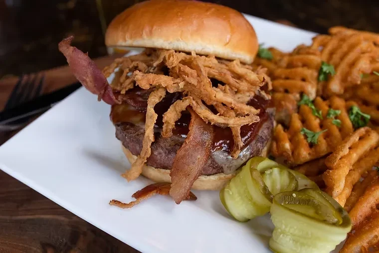 Gourmet burger with bacon, onion strings, waffle fries, and pickles.