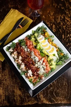 Cobb salad on a white plate with cutlery and a drink.
