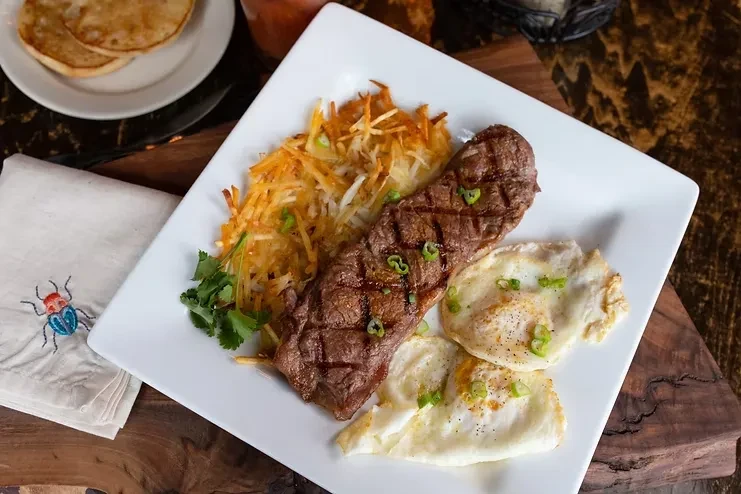 Grilled steak, hash browns, and fried eggs on a white plate.