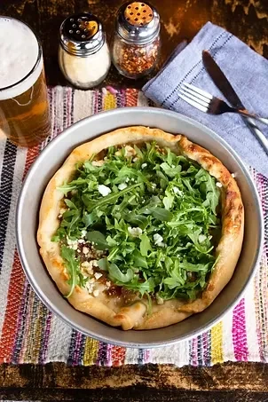 Deep-dish pizza with arugula and cheese, beer, and condiments.
