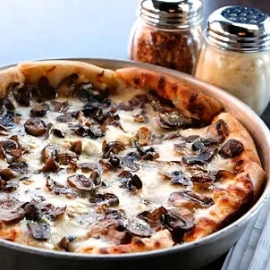Deep-dish pizza with mushrooms, white sauce, and cheese in a pan.