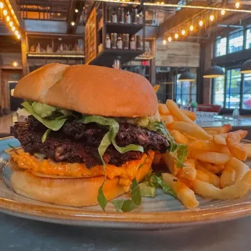 Burger with two patties, lettuce, sauce, and fries on a blue plate.