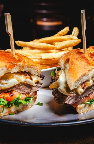 Steak sandwiches with cheese and vegetables, served with fries.