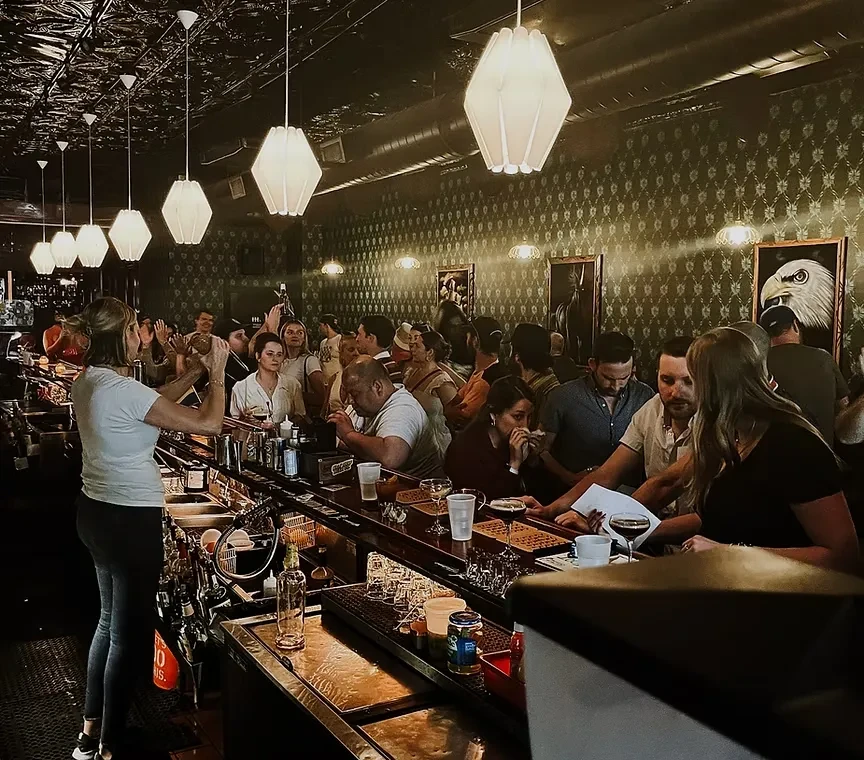 A female bartender mixes drinks in a dim, upscale bar.