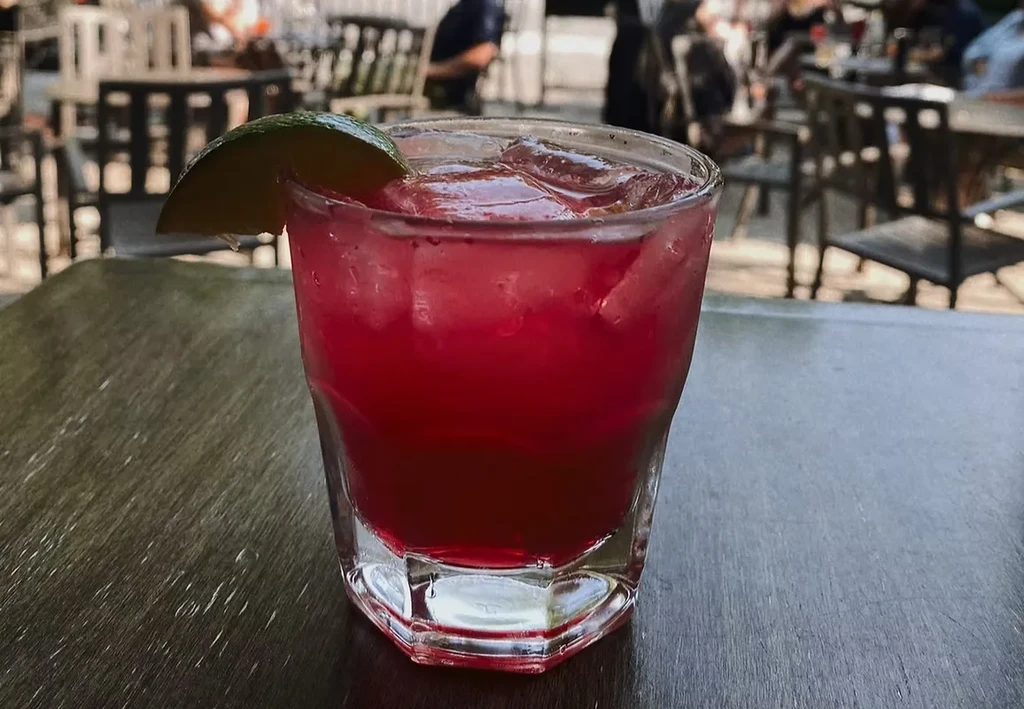 Red-pink cocktail with ice and lime wedge on a wooden table.
