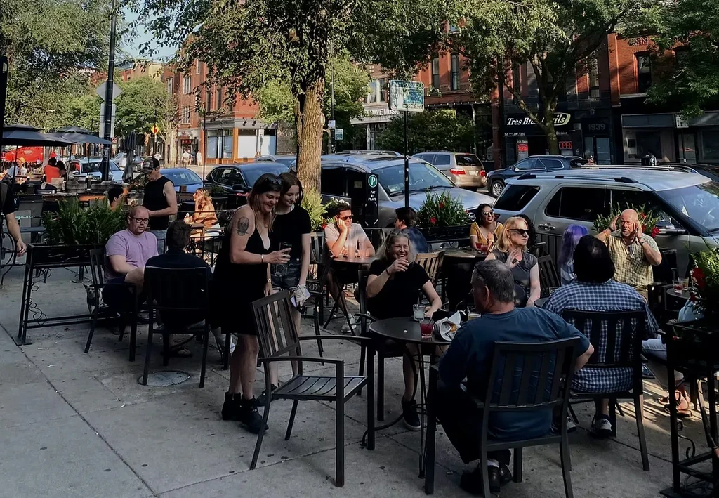 People socializing at a sunny outdoor restaurant patio in an urban setting.