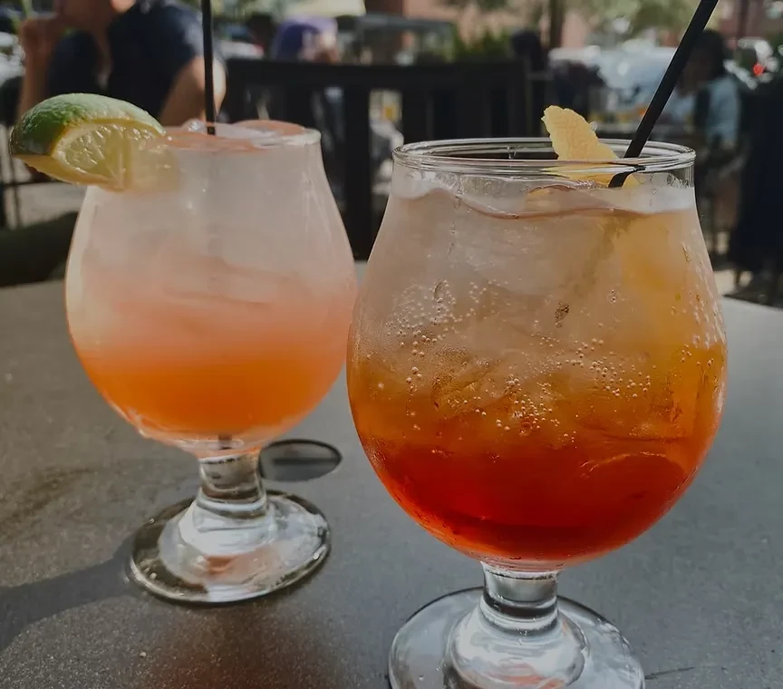 Two cocktails, one pink, one red, with citrus and straws.