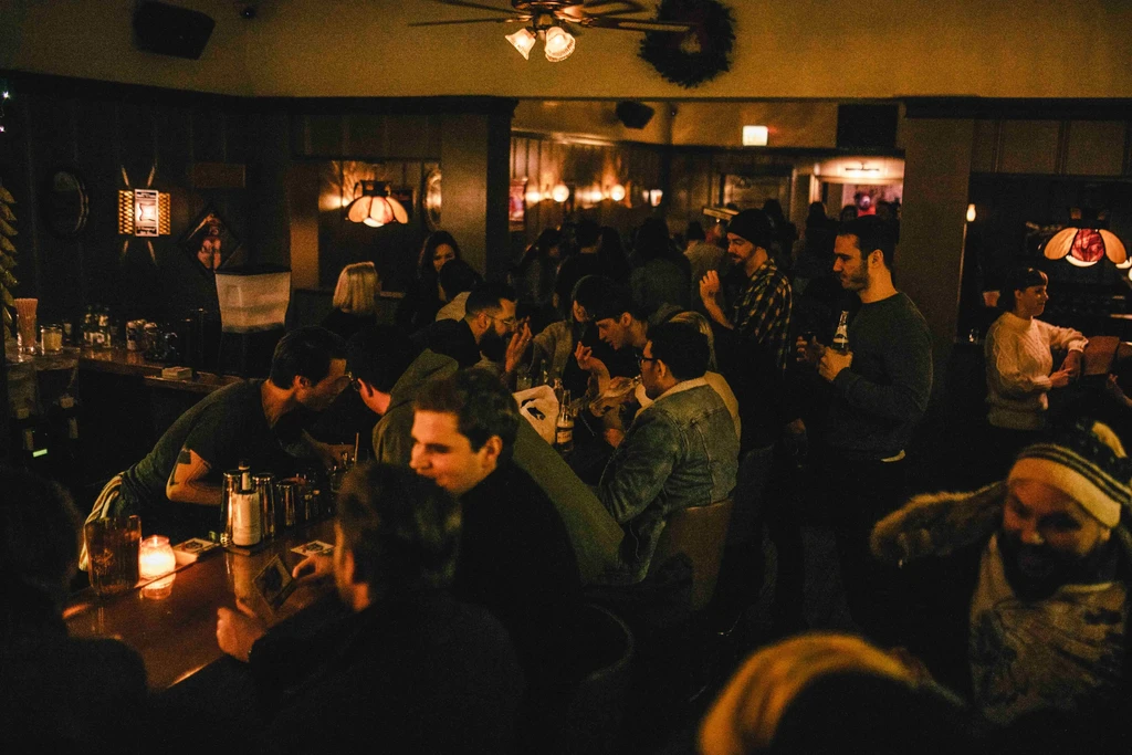 Dimly lit bar filled with people socializing, drinking, and a bartender.