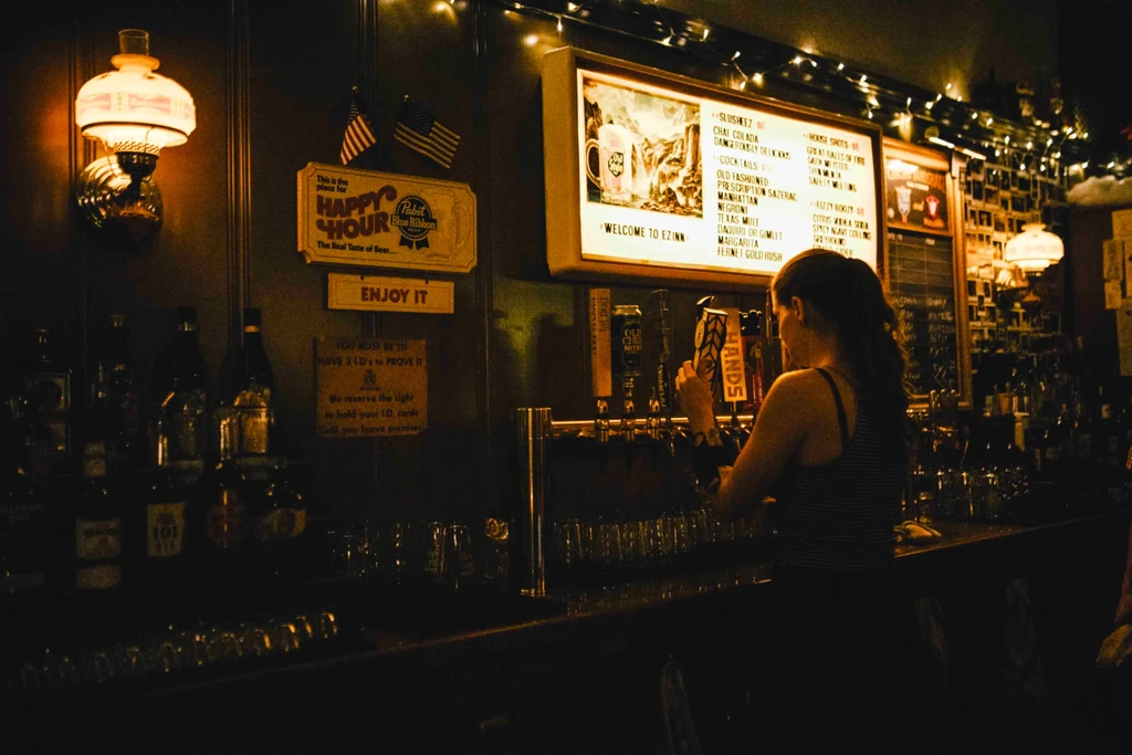 Bartender operates beer taps under an illuminated menu board.