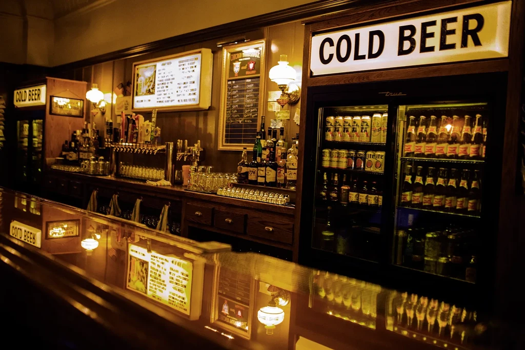 Dimly lit bar with a "COLD BEER" sign and stocked counter.