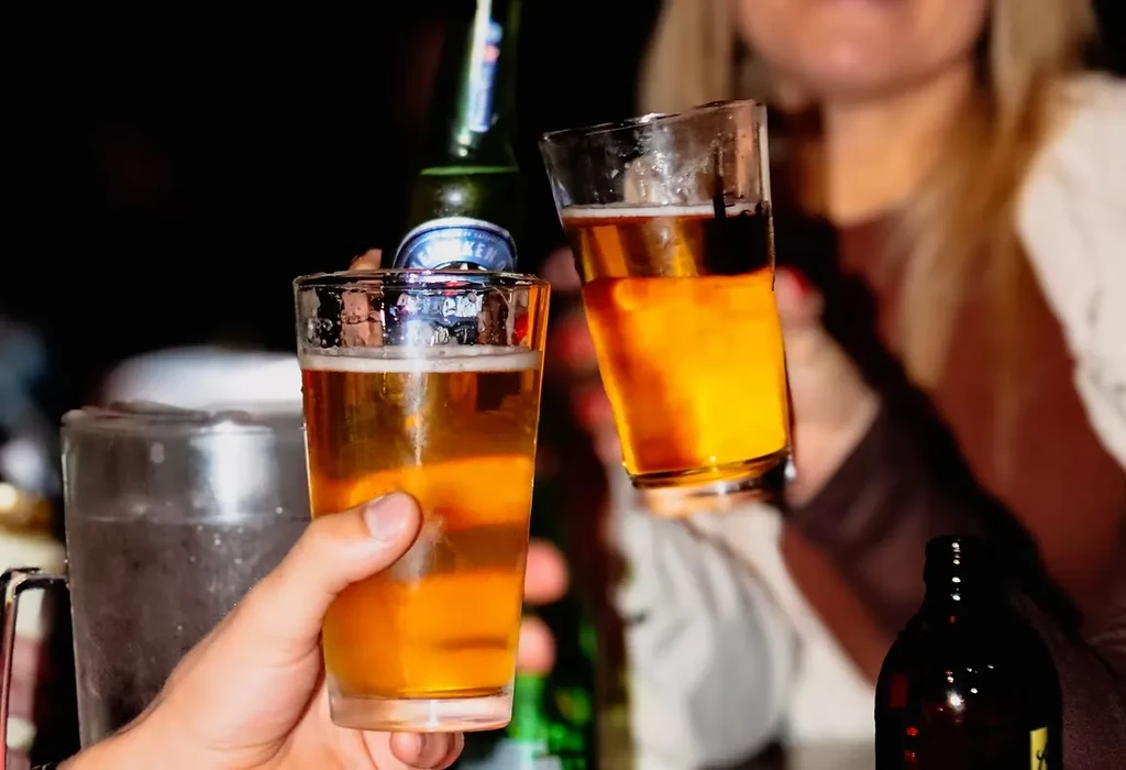 Two clear glasses of amber beer clinking in a toast.