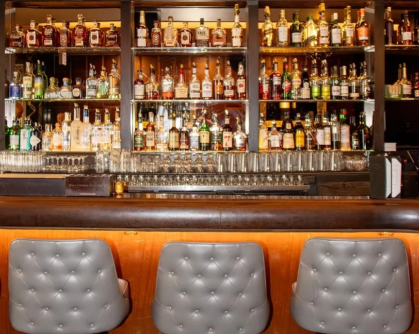 Well-stocked bar with numerous liquor bottles, glasses, and bar stools.