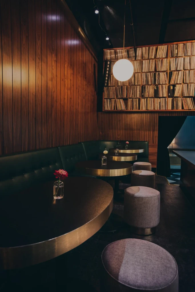 Dimly lit bar with wood paneling, green banquettes, and vinyl records.