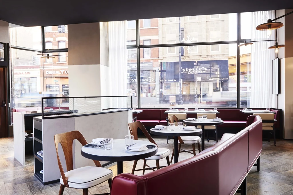 Modern restaurant interior with marble tables, burgundy booths, and street views.