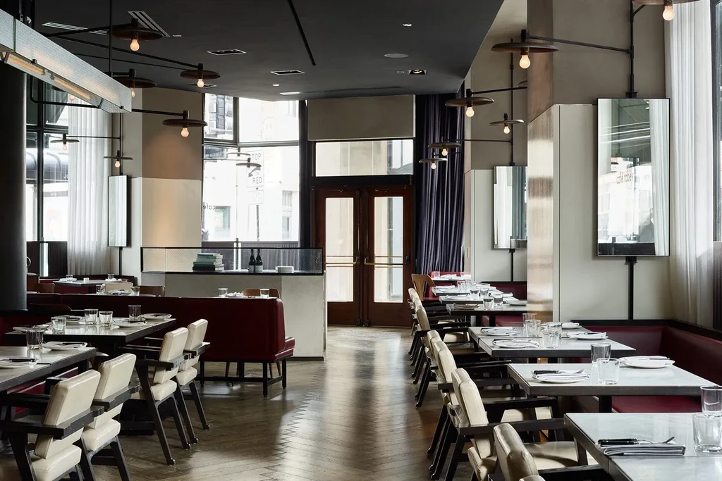 Modern restaurant interior with set tables, booth seating, and industrial lighting.