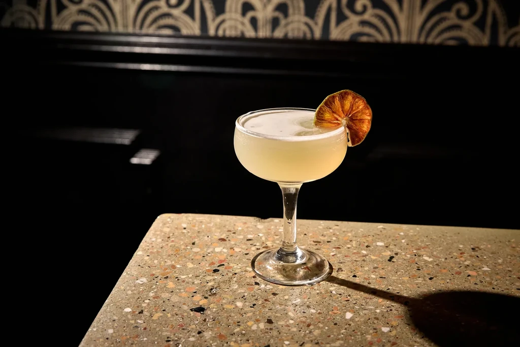 Cocktail in a coupe glass with a dried orange garnish.
