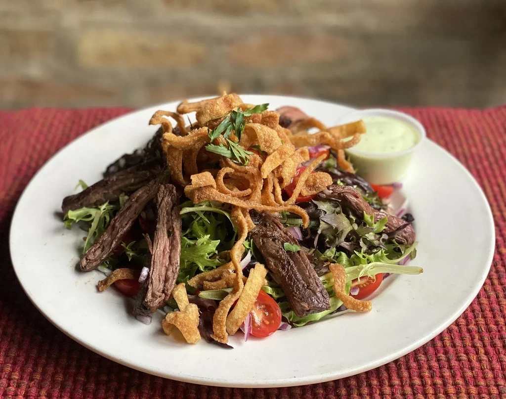 Gourmet salad with mixed greens, steak, tomatoes, fried strips, and dressing.