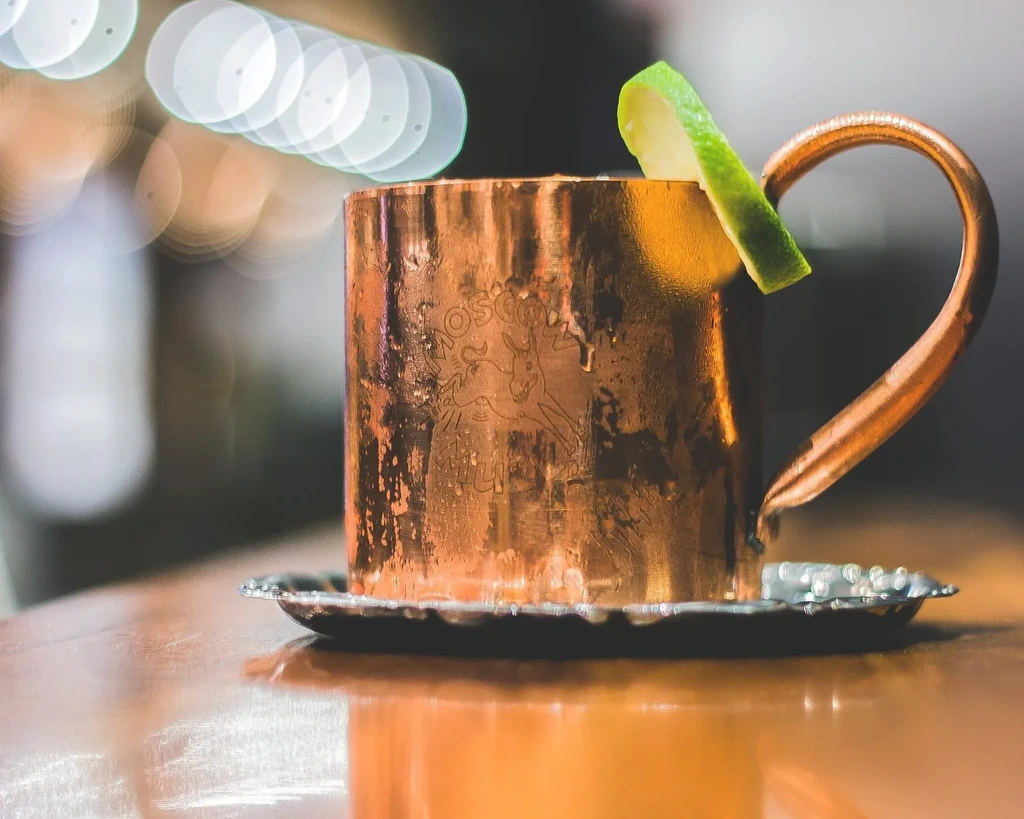 Copper Moscow Mule mug with lime wedge on a wooden surface.