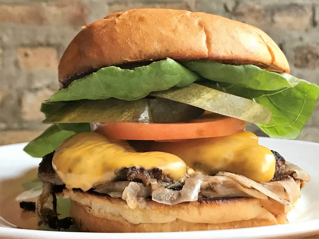 Close-up of a burger with melted cheese, tomato, pickles, and lettuce.