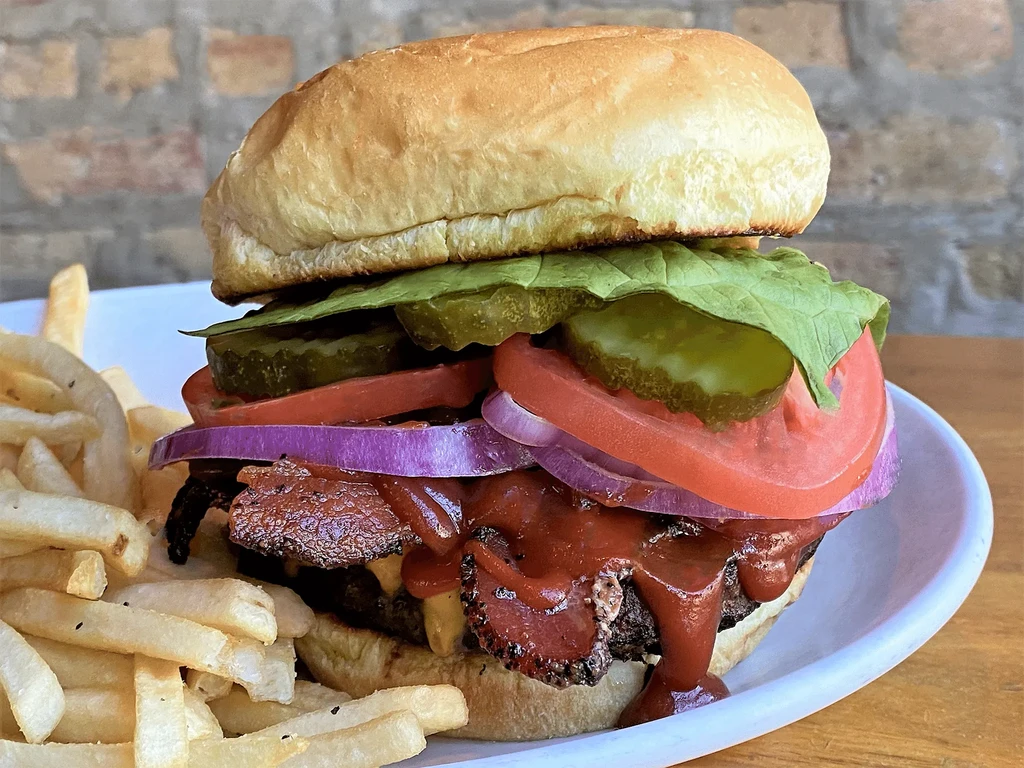 Burger with lettuce, tomato, cheese, bacon, and fries on a plate.