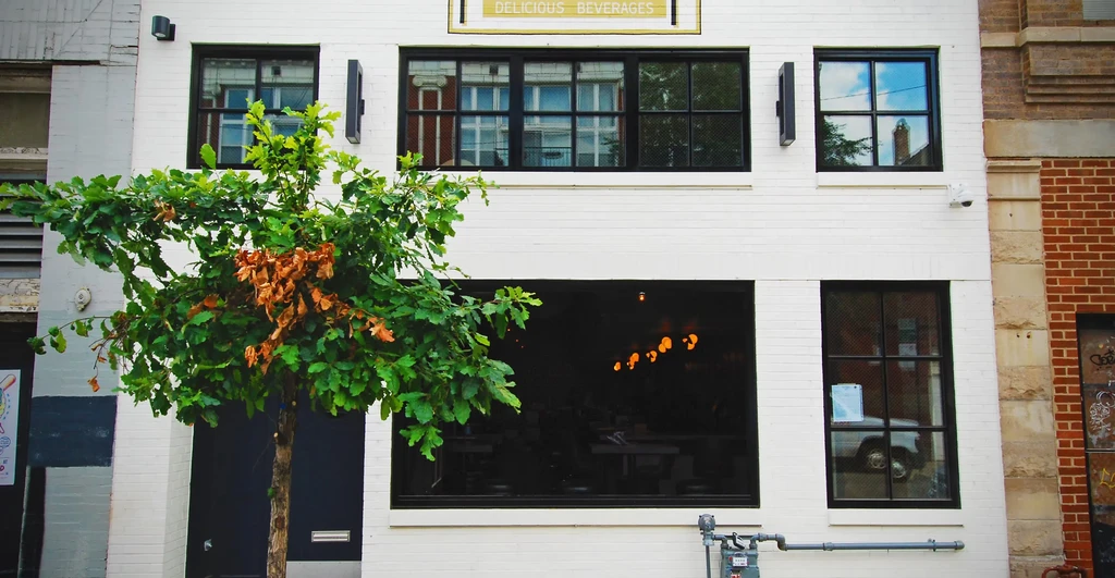 White brick building, "DELICIOUS BEVERAGES" sign, tree in foreground.