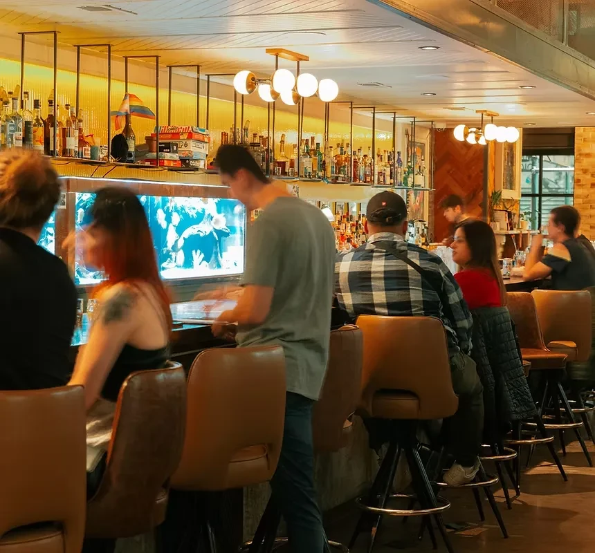 People socialize at a lively bar with glowing shelves and screen.