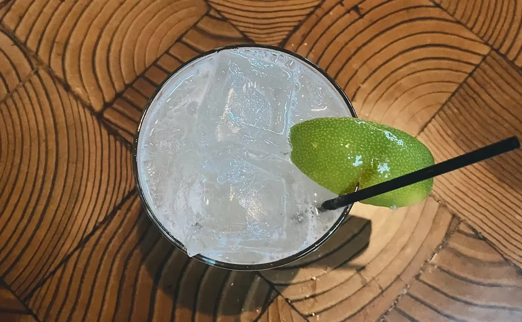 Top-down view of a clear drink with ice, lime, and a straw.