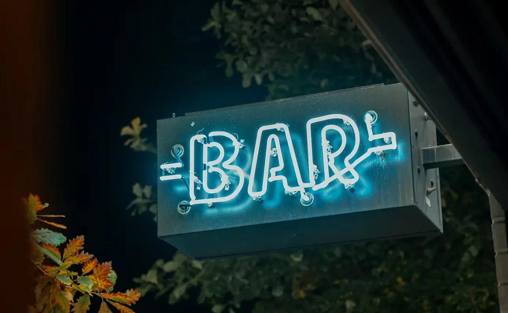 A weathered blue neon sign spells BAR at night.