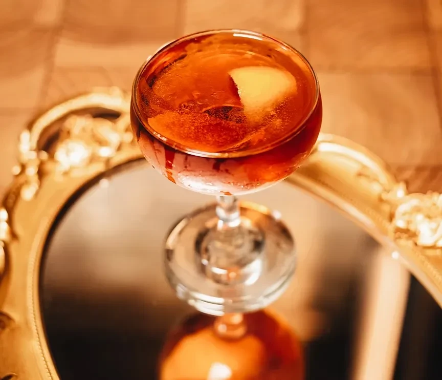 Close-up of an amber cocktail in a coupe glass with citrus peel.