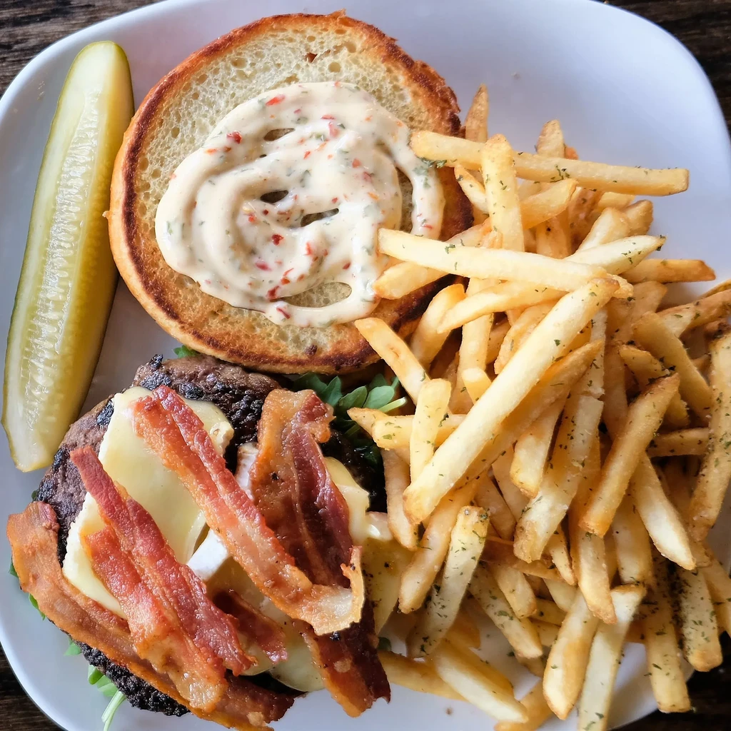Overhead view of a gourmet burger, fries, and a pickle spear.