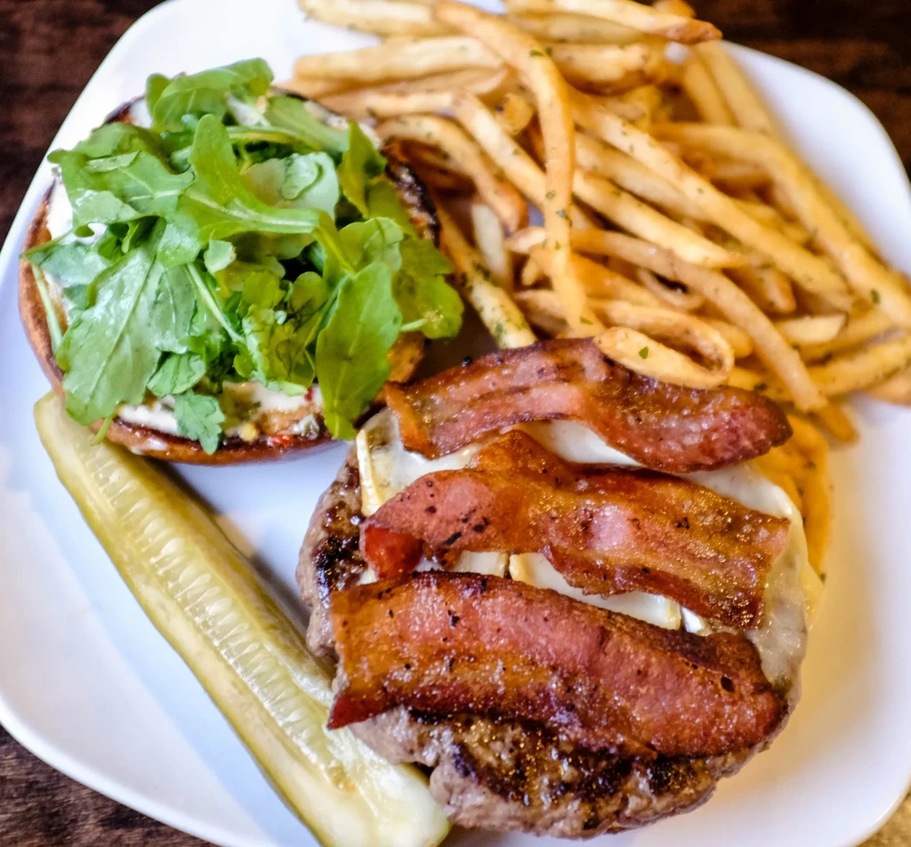 Deconstructed burger, fries, and pickle spear on a white plate.