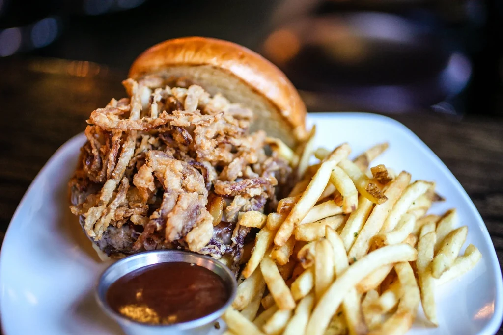 Gourmet burger with crispy onions, french fries, and dipping sauce.