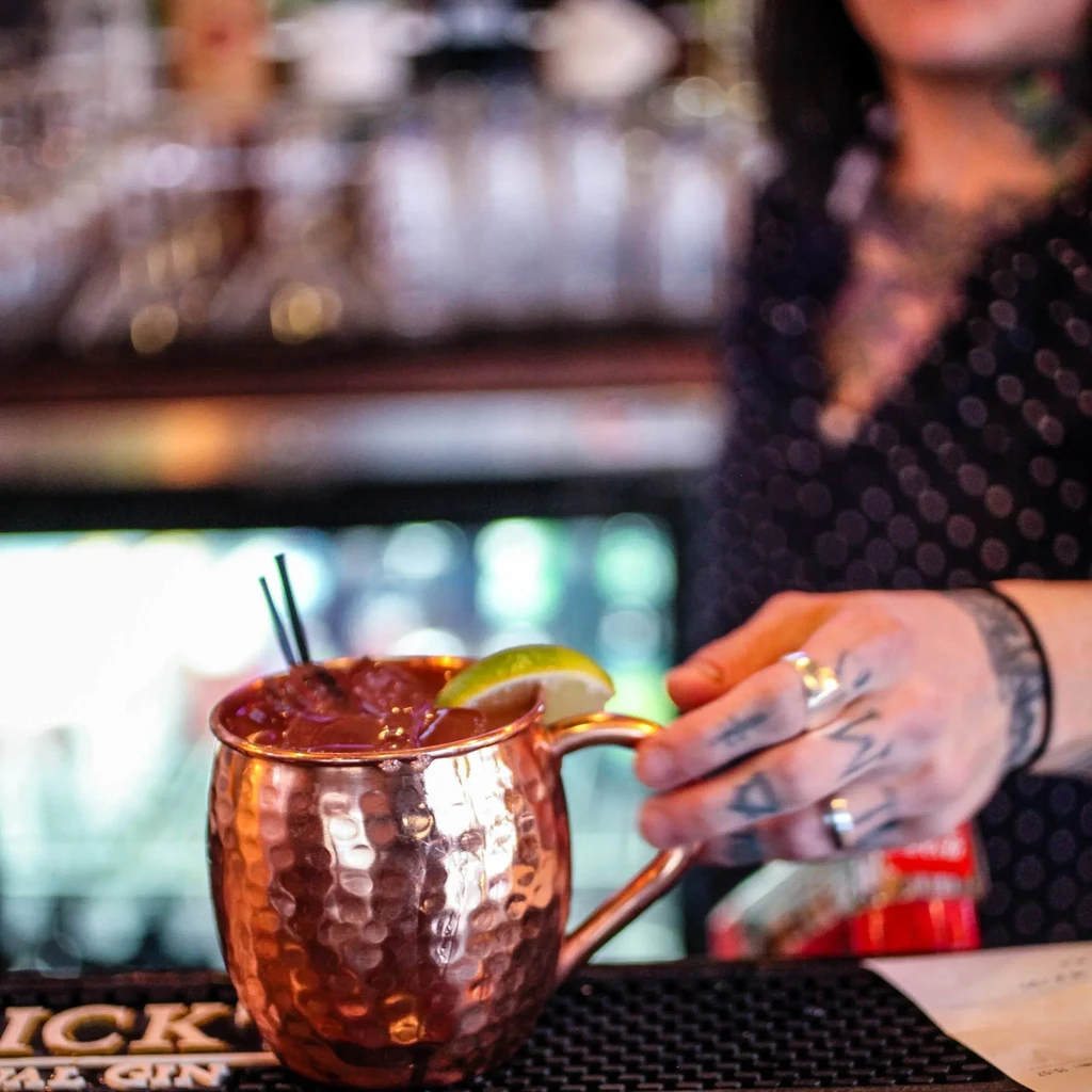 Moscow Mule in copper mug, held by a person with tattoos.