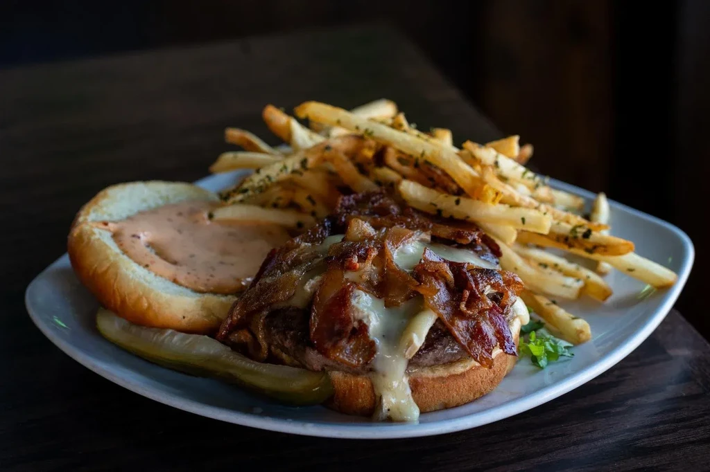 Gourmet open-faced burger with bacon, cheese, caramelized onions, and fries.
