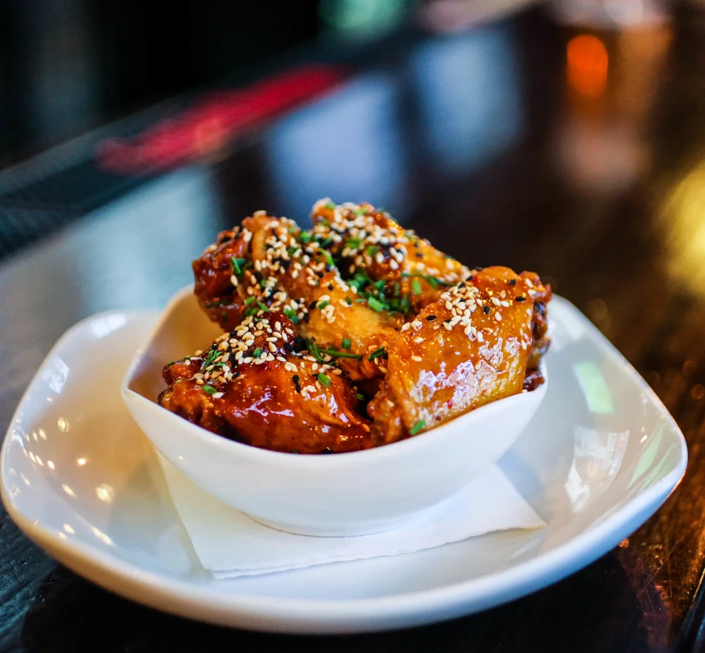 Chicken wings in a white bowl, garnished with sesame seeds and chives.