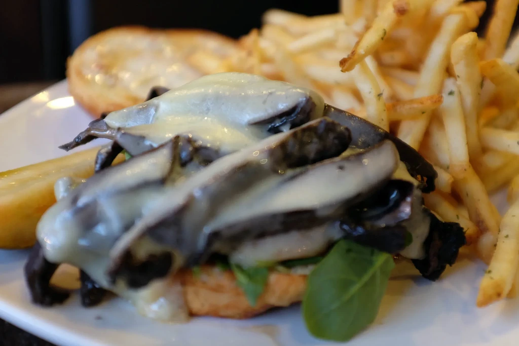 Open-faced sandwich with mushrooms, melted cheese, fries, and a pickle.