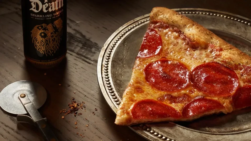 A slice of pepperoni pizza on a silver plate with sparkling water.