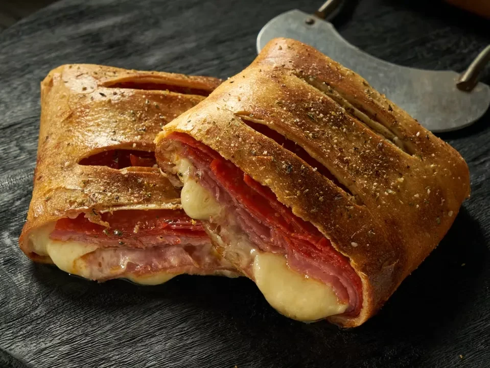 Savory pastry or stromboli, cut in half, with meat and cheese.