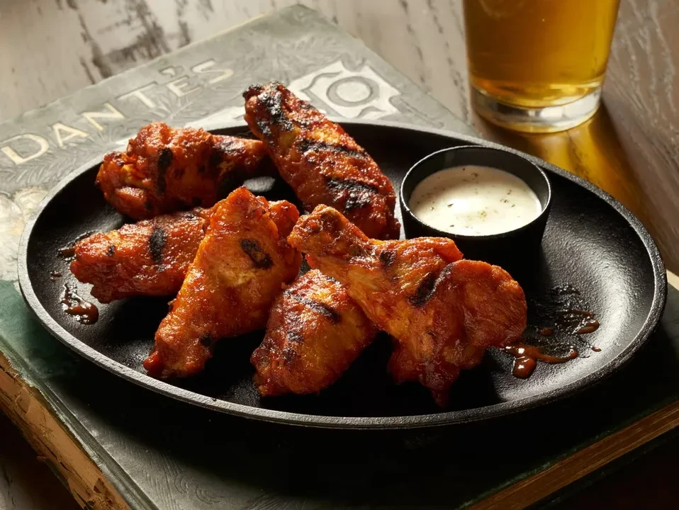 Grilled chicken wings with dipping sauce and beer on stacked books.