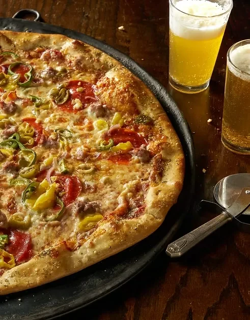 Pizza on black pan with beer and pizza cutter.