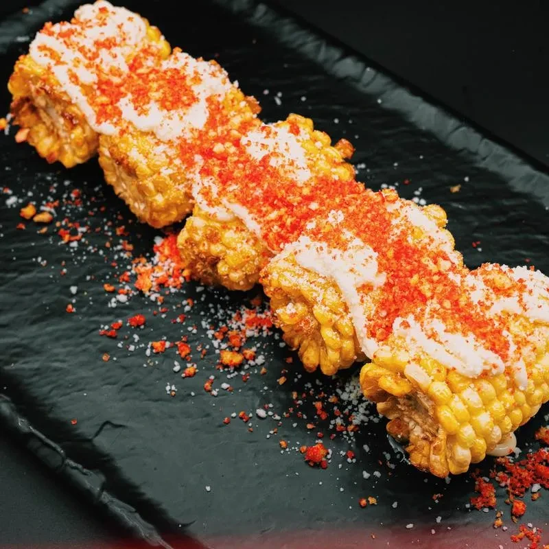 Four pieces of elote, topped with sauce, chili powder, and cheese.
