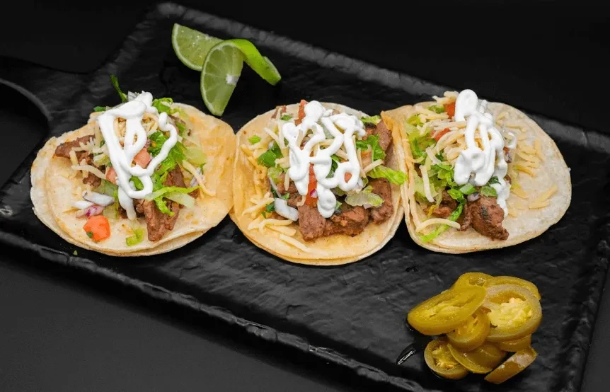 Three soft-shell tacos with meat, cheese, lettuce, and lime.