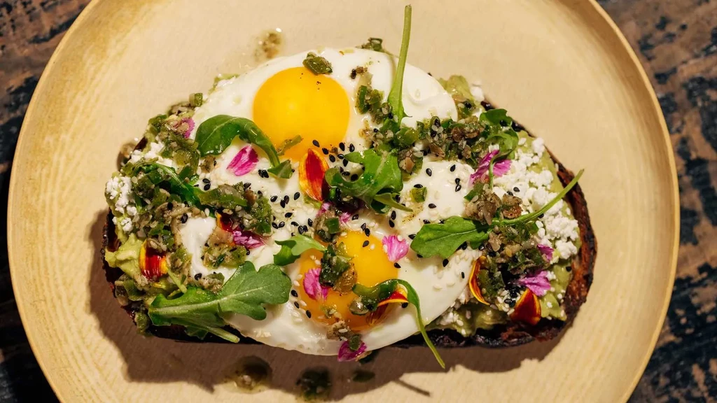 Avocado toast with fried eggs, cheese, arugula, and edible flowers.