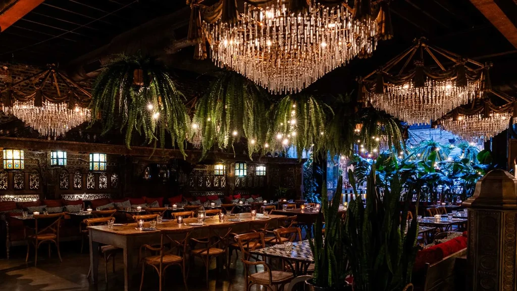 Dimly lit restaurant interior with ornate chandeliers, plants, and set tables.
