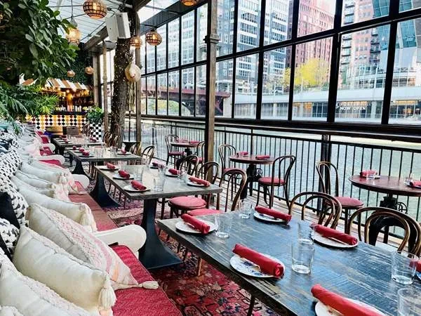 Restaurant interior with banquette seating, city view, and river reflection.