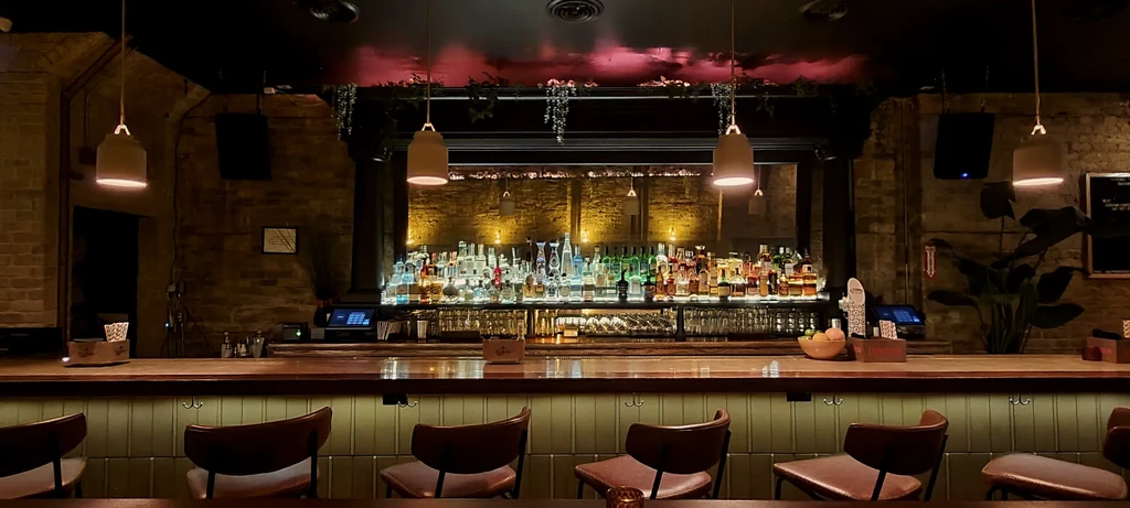 A well-lit, fully stocked bar with wooden counter and brick walls.