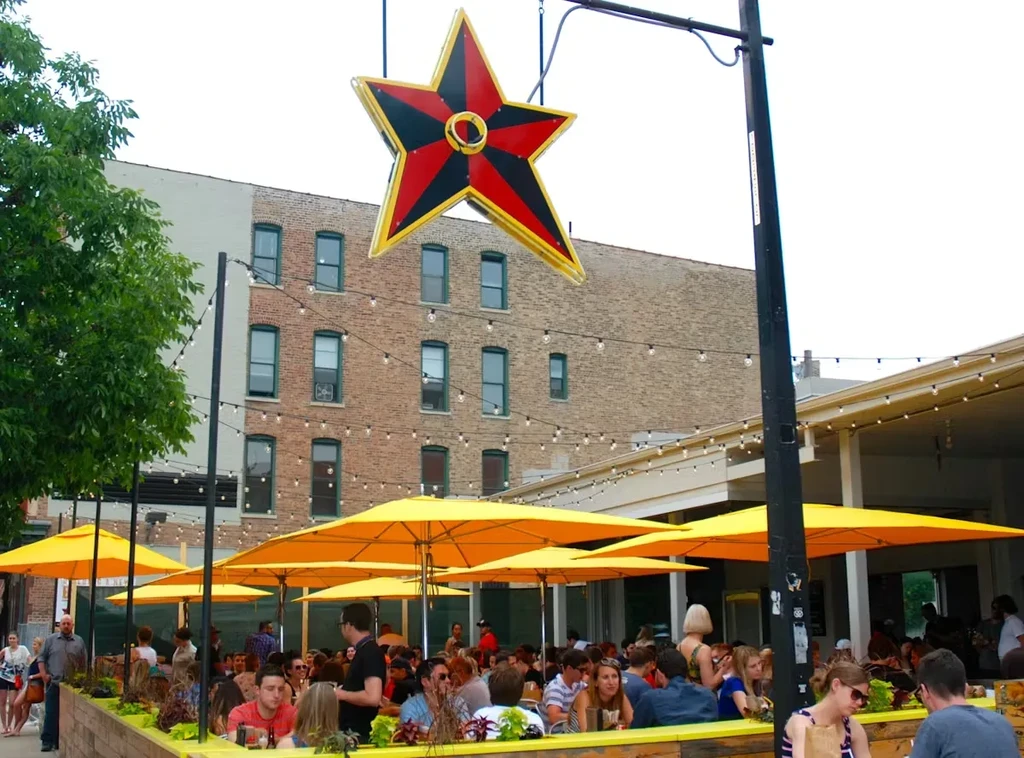 Restaurant patio with yellow umbrellas, market lights, and people.