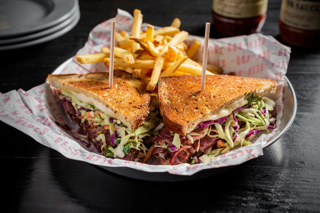 Reuben sandwich halves and french fries in a metal bowl.