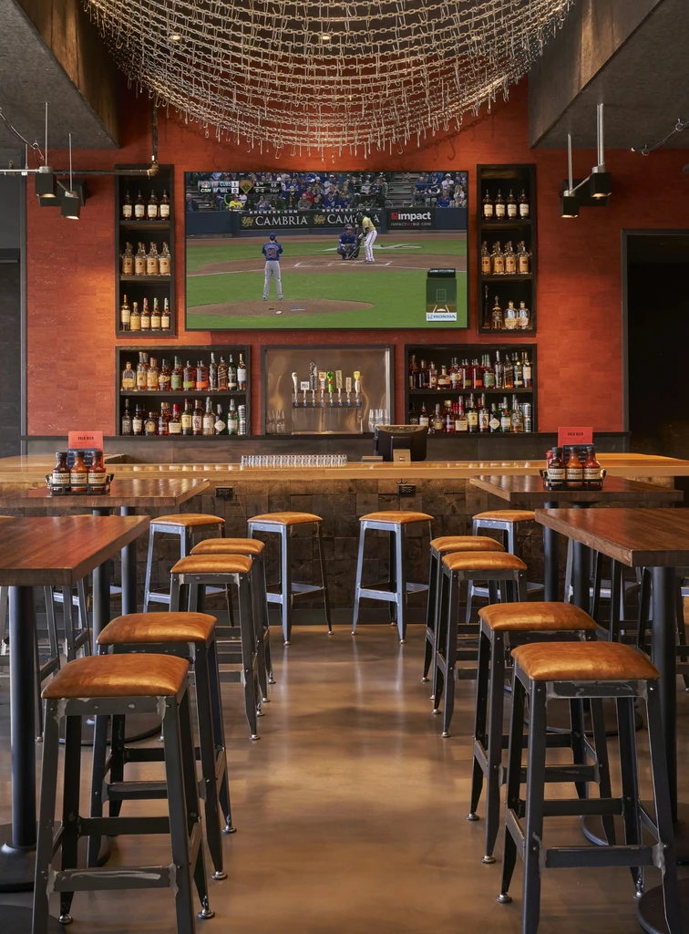 Modern bar interior with baseball game on TV, liquor bottles, and seating.